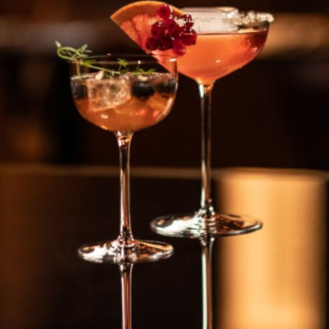 SC Hospitality Tone small cocktail coupe glasses filled with vibrant cocktails, garnished with fruit and herbs.