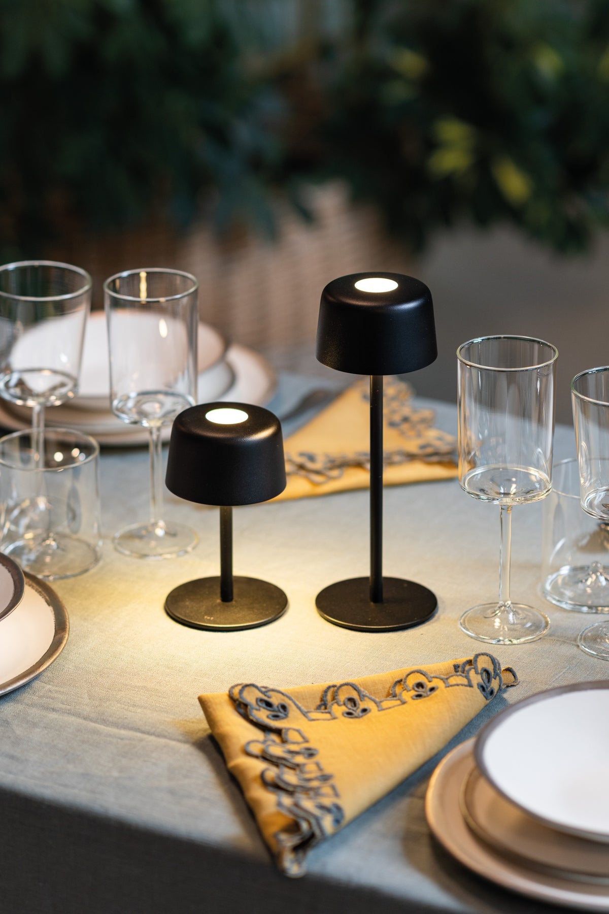 Two SC Hospitality Ailati 1+1 black metal cordless table lamps illuminating a dining table setting.