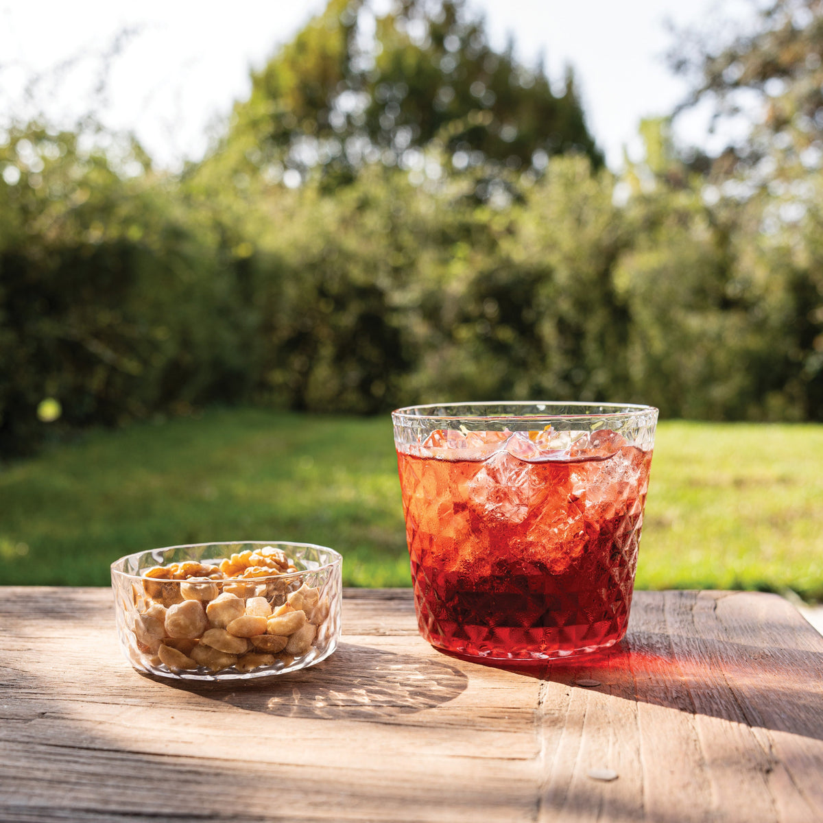 SC Hospitality Zafferano Mixology 8.5cm glass bowl filled with nuts next to a cocktail on a wooden outdoor table
