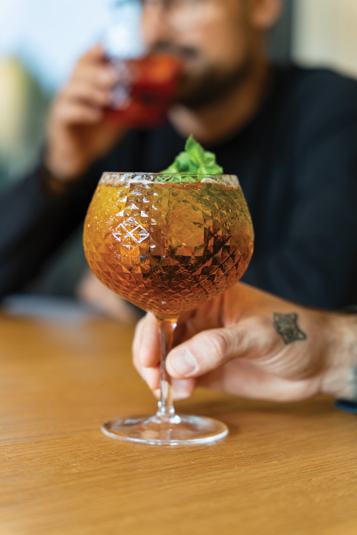SC Hospitality Mixology goblet balloon glass with geometric texture holding an amber cocktail on a wooden table