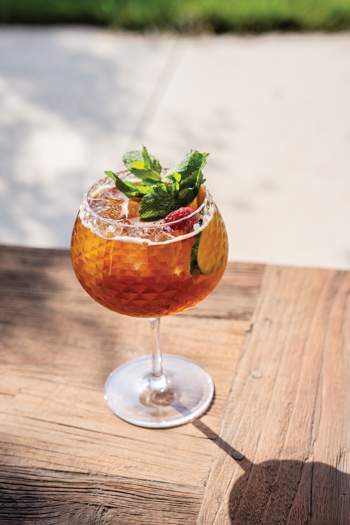 SC Hospitality Mixology goblet balloon glass with geometric texture filled with an amber cocktail, mint, and fruit.