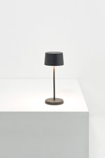 SC Hospitality Olivia Micro cordless dark grey table lamp with a slim stem and warm LED glow on a white surface.
