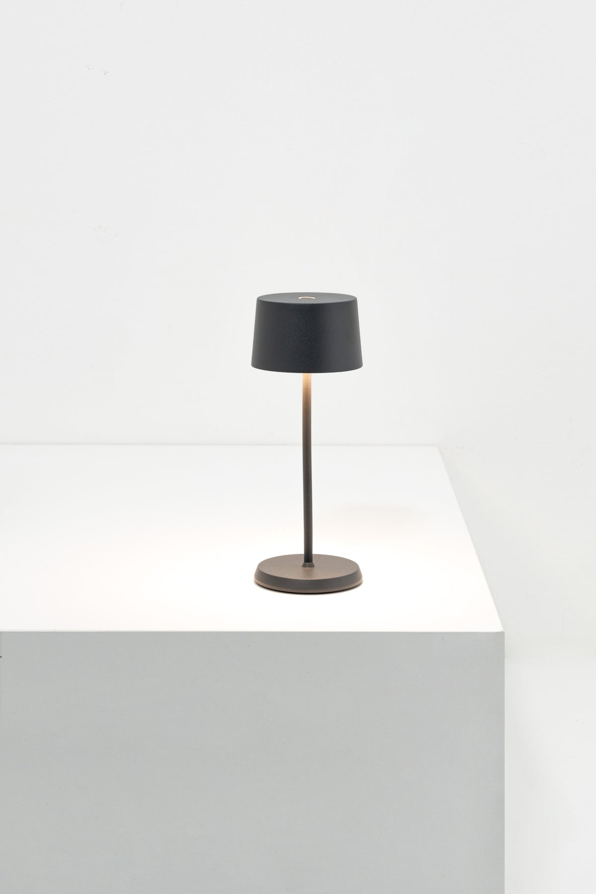 SC Hospitality Olivia Micro cordless dark grey table lamp with a slim stem and warm LED glow on a white surface.
