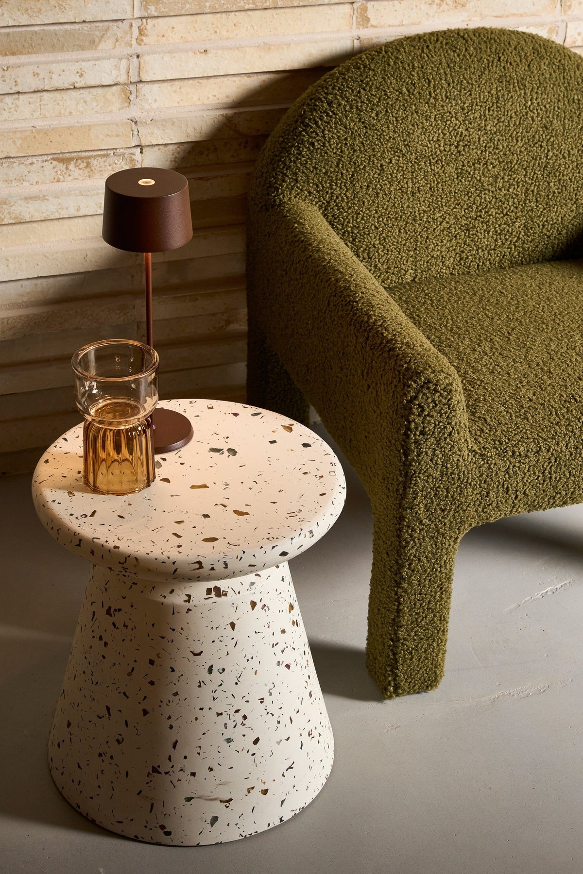 SC Hospitality Olivia Pro cordless table lamp in corten finish on a terrazzo side table next to a green armchair