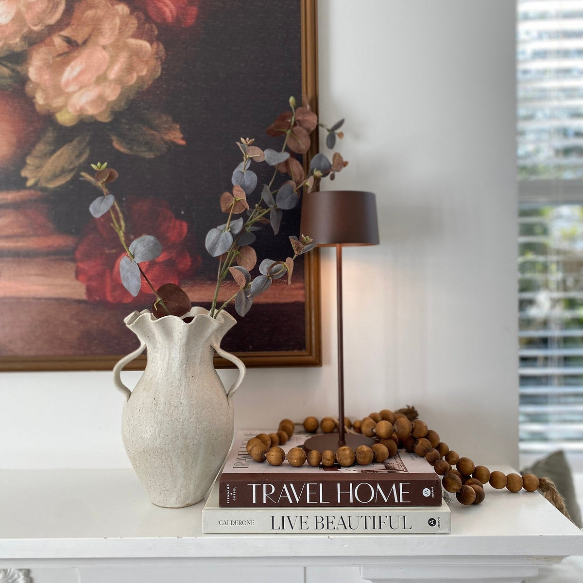 SC Hospitality Olivia Pro cordless table lamp in corten finish, styled on a shelf with books and a decorative vase.