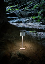 SC Hospitality Olivia Pro white cordless LED table lamp glowing on a rocky outdoor surface
