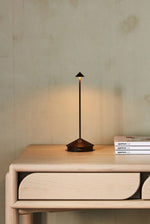 SC Hospitality Pina cordless table lamp in corten finish, featuring a sleek minimalist design on a wooden table.