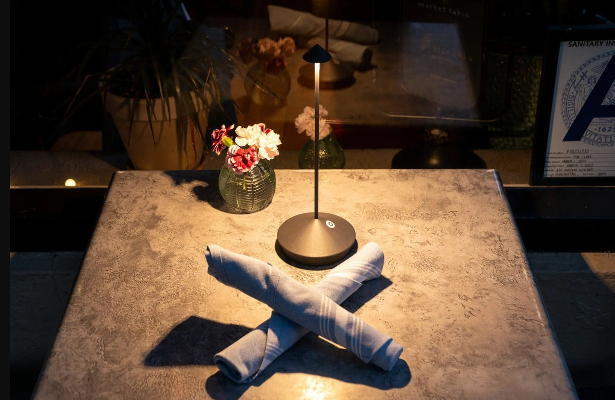 SC Hospitality Pina dark grey cordless rechargeable LED table lamp on a restaurant table with napkins and flowers