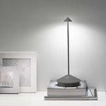 SC Hospitality Pina cordless dark grey table lamp with a sleek, minimalist design glowing on a stack of books.