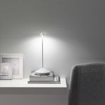 SC Hospitality Pina white cordless rechargeable table lamp glowing on a stack of books on a white shelf