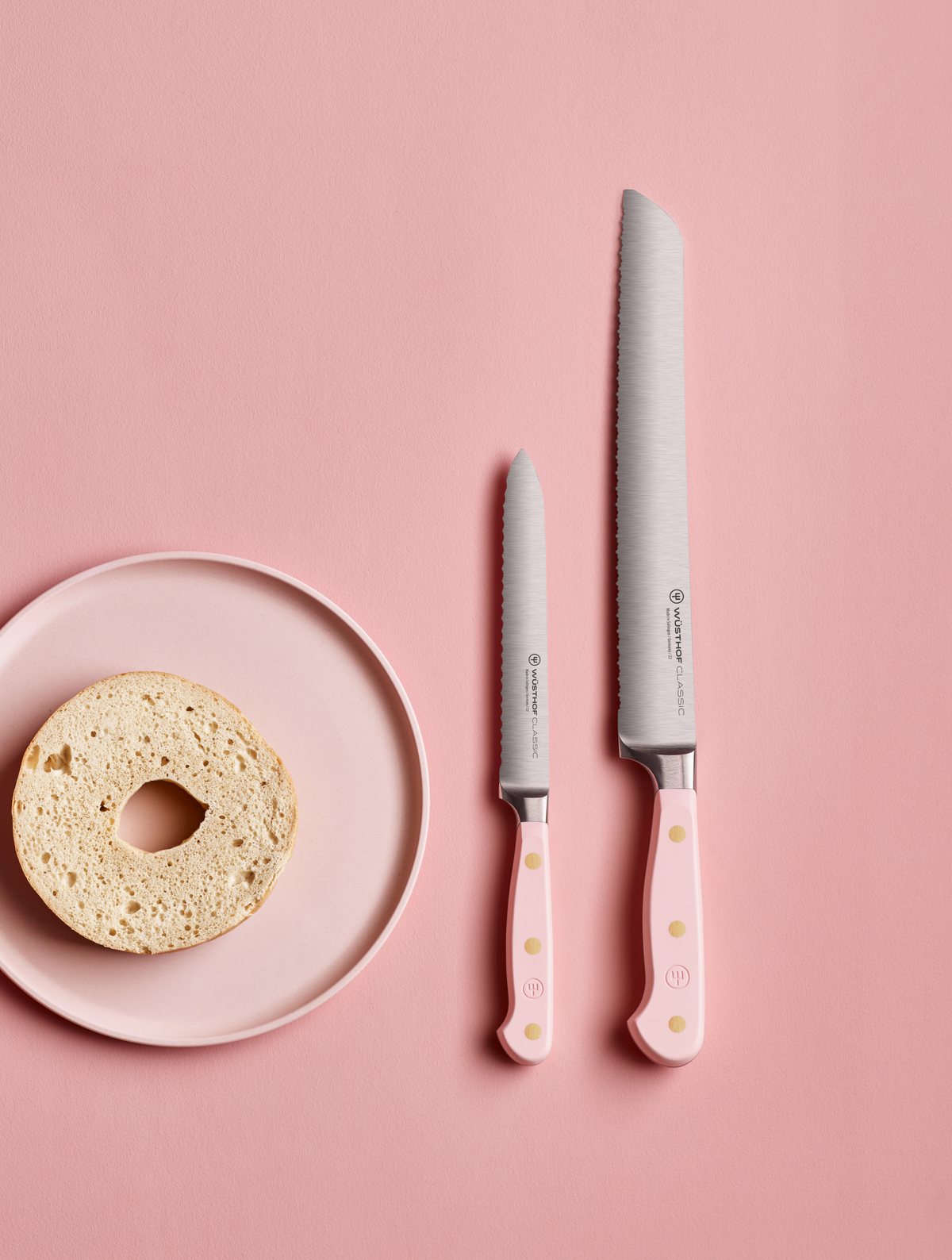 SC Hospitality WÜSTHOF bread and utility knives with pink Himalayan salt handles next to a bagel on a pink plate.