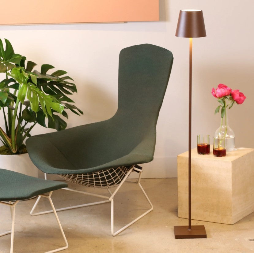SC Hospitality Poldina Pro cordless floor lamp in corten finish standing next to a green lounge chair and side table.