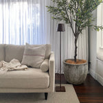SC Hospitality Poldina Pro cordless floor lamp in corten finish standing next to a cream sofa and potted olive tree