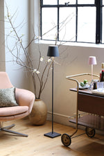 SC Hospitality Poldina Pro dark grey cordless floor lamp standing in a bright living room next to a pink armchair.