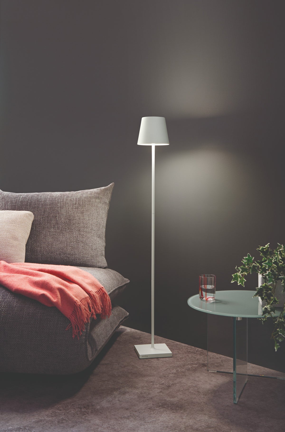 SC Hospitality white Poldina Pro cordless floor lamp illuminating a modern living room corner with a grey sofa.