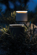 SC Hospitality Push-Up table lamp in sand finish glowing softly in a garden setting at night