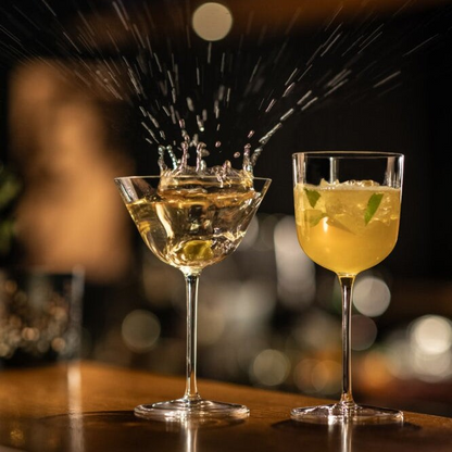 SC Hospitality Tone Martini glass with a cocktail splash next to a small cocktail coupe on a bar counter