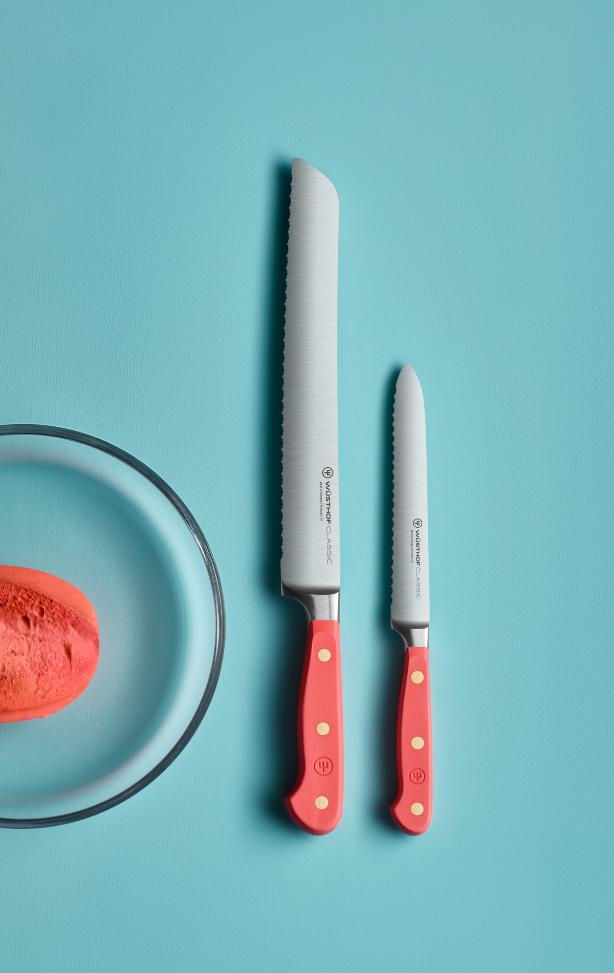 SC Hospitality Wüsthof Classic coral peach serrated bread knives with stainless steel blades on a blue background.
