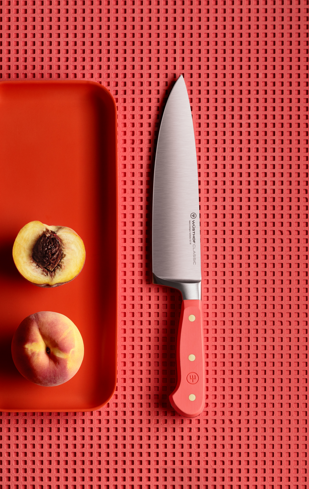SC Hospitality Wüsthof 20cm cooks knife with coral peach handle and stainless steel blade next to fresh peach halves.