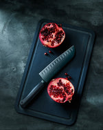 SC Hospitality WÜSTHOF Performer 17cm Santoku knife with black DLC coating and textured handle next to a pomegranate.