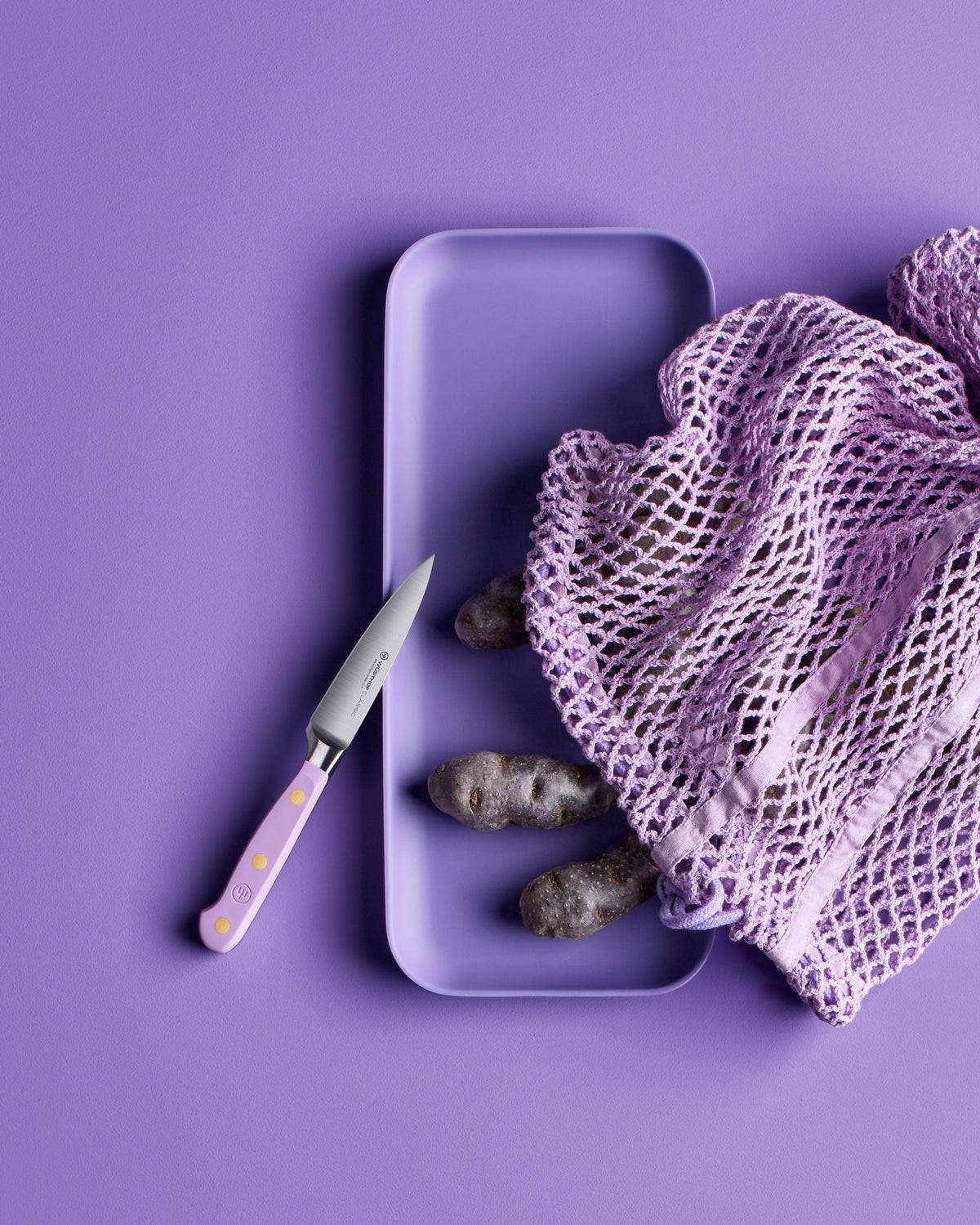 SC Hospitality Wüsthof 9cm paring knife with purple yam handle next to a mesh bag of purple potatoes on a purple tray