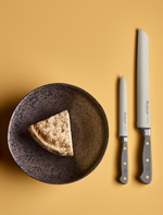 SC Hospitality Wüsthof Velvet Oyster serrated bread knife and paring knife next to a slice of cheese on a rustic plate