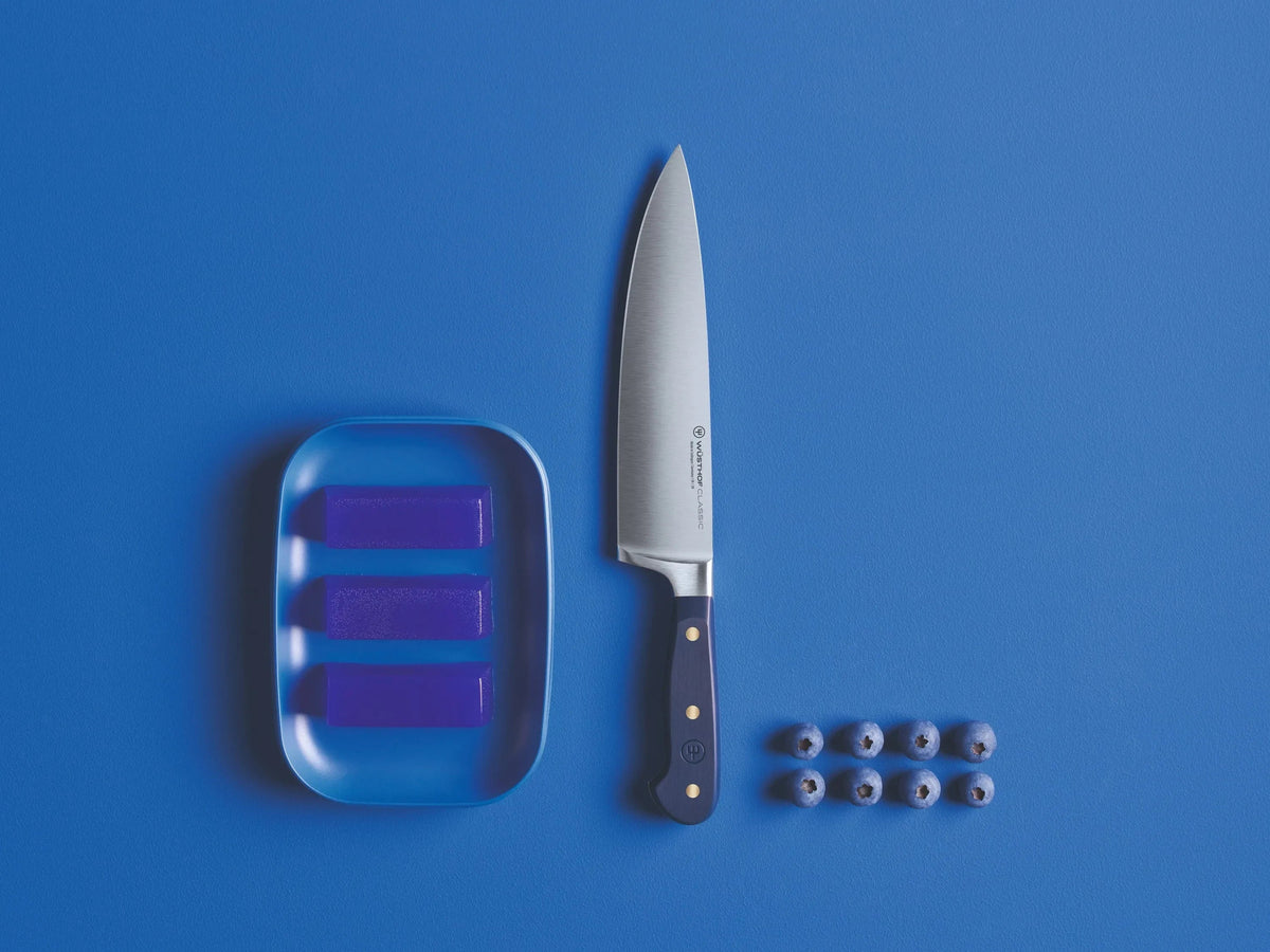 SC Hospitality Wüsthof 16cm cooks knife with a Wild Blueberry synthetic handle on a blue background with blueberries.
